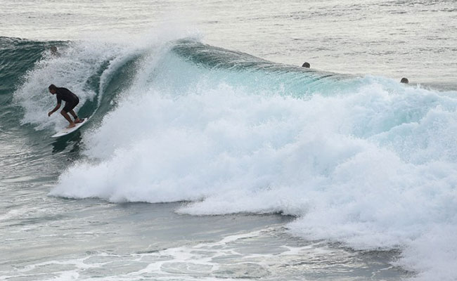 Surfer makes way over rocks to surf at Boulders Beach in Ballina in northern New South Wales. (AFP Image)