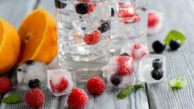 a cup of water filled with ice and berries and in a place filled with fruits